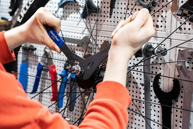 Eine Hand benutzt ein Werkzeug aus dem Fahrrad-Werkzeugkoffer zur Wartung eines Mountainbikes in einer Werkstatt.