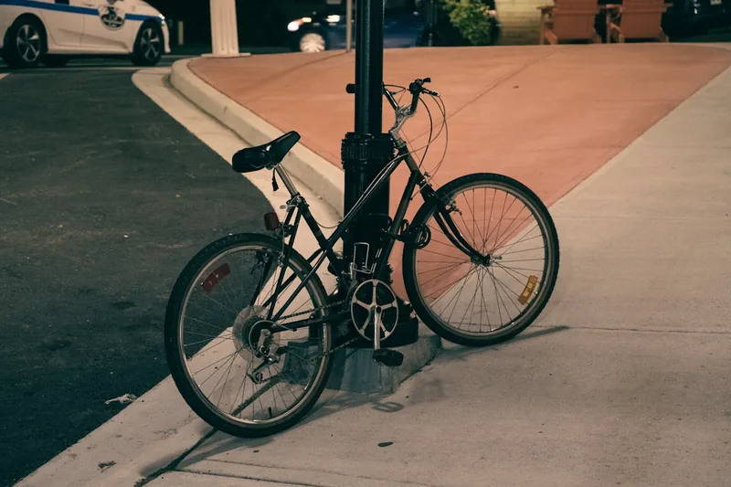 Eine Person sichert ein Fahrrad mit einem robusten Kettenschloss an einem Fahrradständer im städtischen Umfeld.