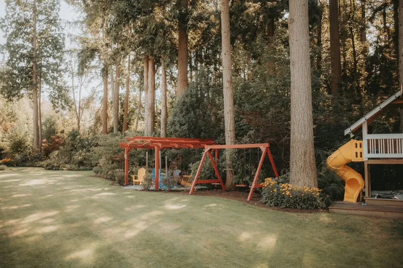 Ein idyllischer Garten mit einem Spielturm im Hintergrund, spielende Kinder und entspannte Eltern.
