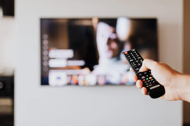 Eine Hand navigiert mit einer Fernbedienung durch Smart-TV-Apps auf einem 28-Zoll-Fernseher, symbolisch für die Nutzung.