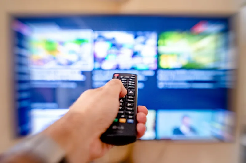 Person bedient 55-Zoll-4K-Fernseher mit Fernbedienung und genießt Entertainment im modernen Wohnzimmer.