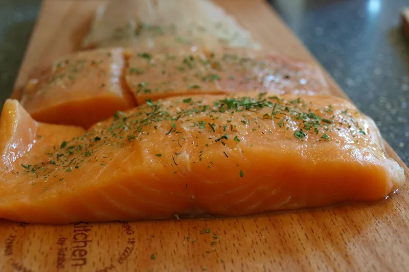 Eine Person befestigt einen Lachs auf dem Flammlachsbrett am Grill über offener Flamme.