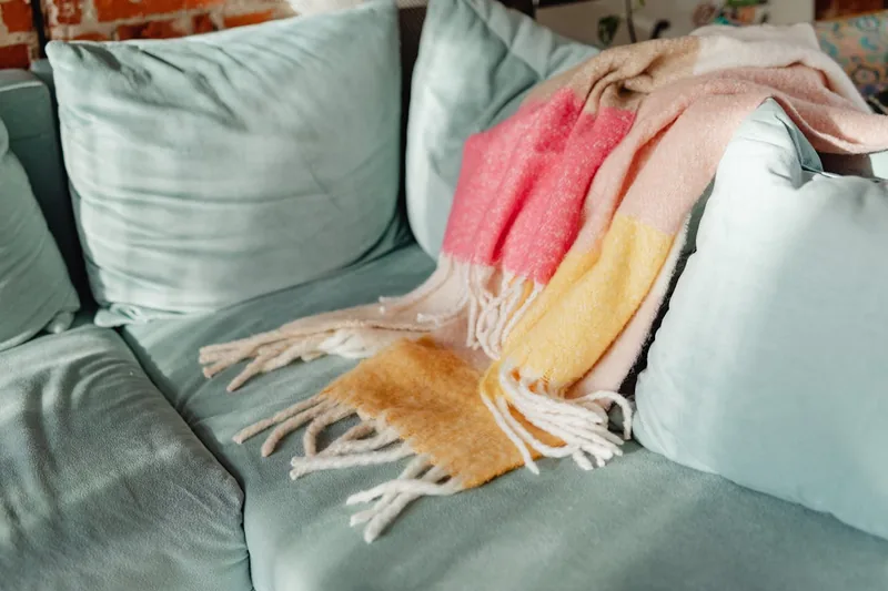 Gemütliches Wohnzimmer mit einer Fleecedecke elegant über einem Sofa drapiert, Abendstimmung.