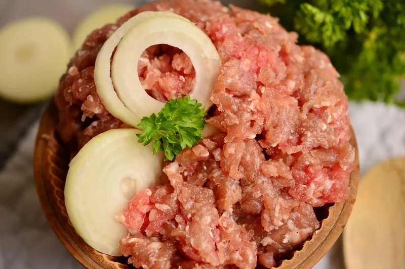 Eine Schüssel mit frisch gewolftem Hackfleisch und Gewürzen auf einer Küchentheke.