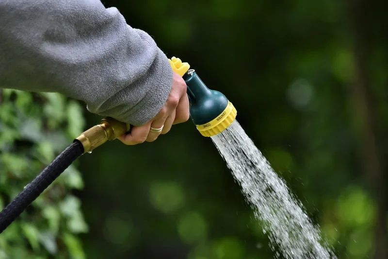 Eine Person bewässert Pflanzen im Garten mit einem flexiblen Gartenschlauch, der sich beim Gebrauch ausdehnt.