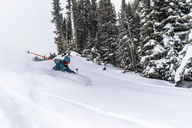 Ein Freerider in voller Montur, wie er mit seinen Freeride-Ski durch frischen Tiefschnee gleitet, seitliche Ansicht.