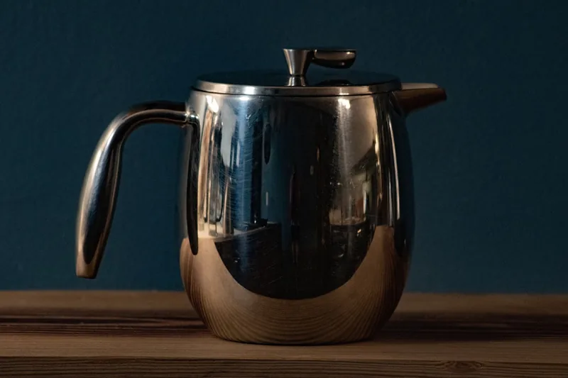 Eine Hand drückt den Stempel eines French Press Kaffeebereiters herunter, frischer Kaffee.