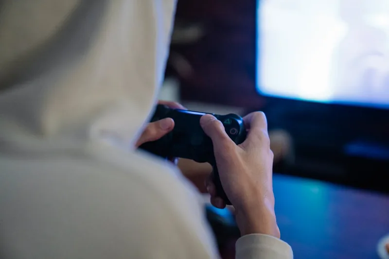 Hände halten einen Controller, spielen ein actionreiches Videospiel auf einem großen 4K Gaming Monitor.