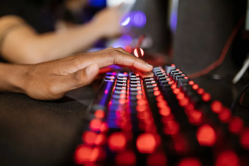 Eine Person spielt konzentriert ein Videospiel auf einem Gaming Notebook, Hände auf Tastatur und externer Maus.