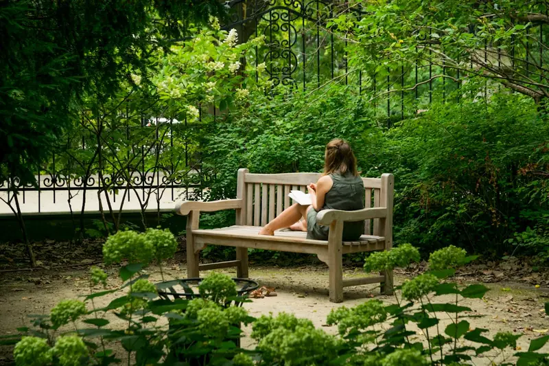 Eine Person entspannt auf einer modernen Gartenbank, liest ein Buch im Grünen.