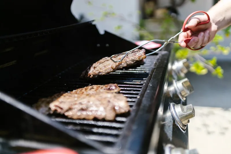 Fröhliche Grillparty im Garten mit Freunden, der Gasgrill im Hintergrund sorgt für leckeres Essen.