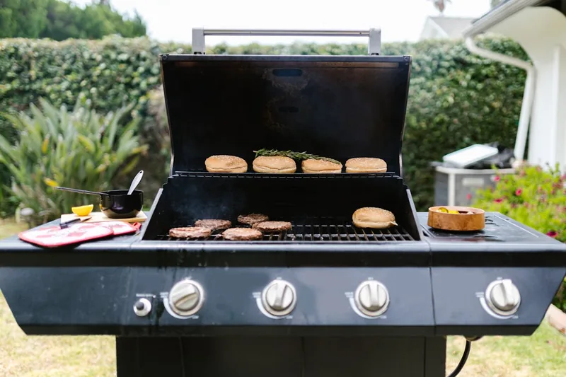 Ein reich gedeckter Tisch im Garten mit frisch gegrilltem Essen und fröhlicher Atmosphäre unter freiem Himmel.