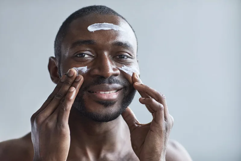 Ein Mann trägt vorsichtig eine Gesichtscreme für Männer auf sein Gesicht auf, sichtbare Hand.