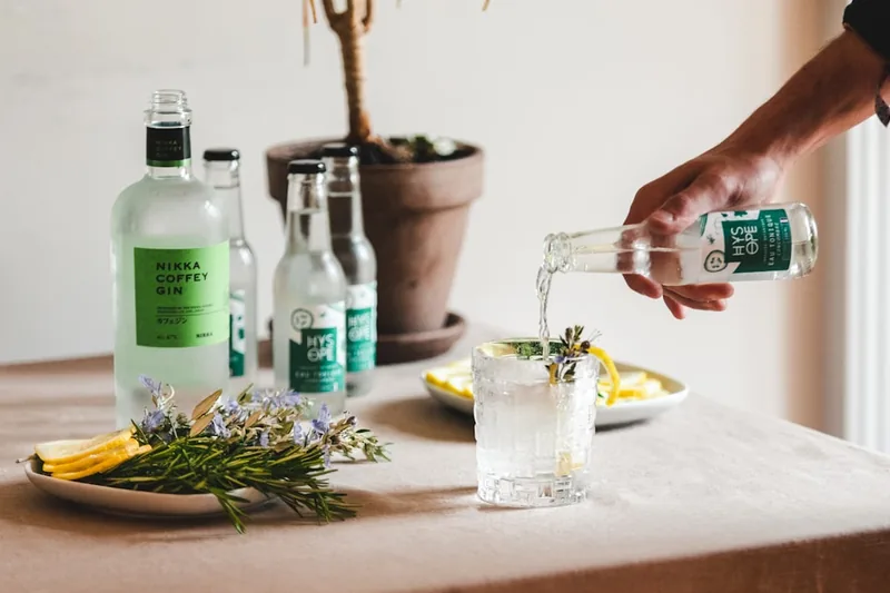 Eine Person bereitet sorgfältig einen Gin Tonic zu, indem sie Gin in ein mit Eis gefülltes Glas gießt.
