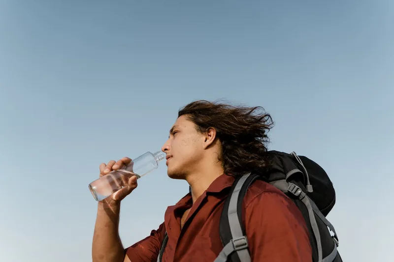 Eine Person trinkt Wasser aus einer Glas-Trinkflasche während einer Wanderung in der Natur.