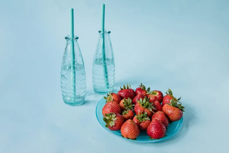 Idyllische Picknick-Szene im Park mit einer Glas-Trinkflasche neben frischem Obst und Büchern.