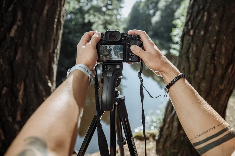 Eine Person befestigt ein flexibles Stativ mit einem Smartphone an einem Ast in einem Wald.