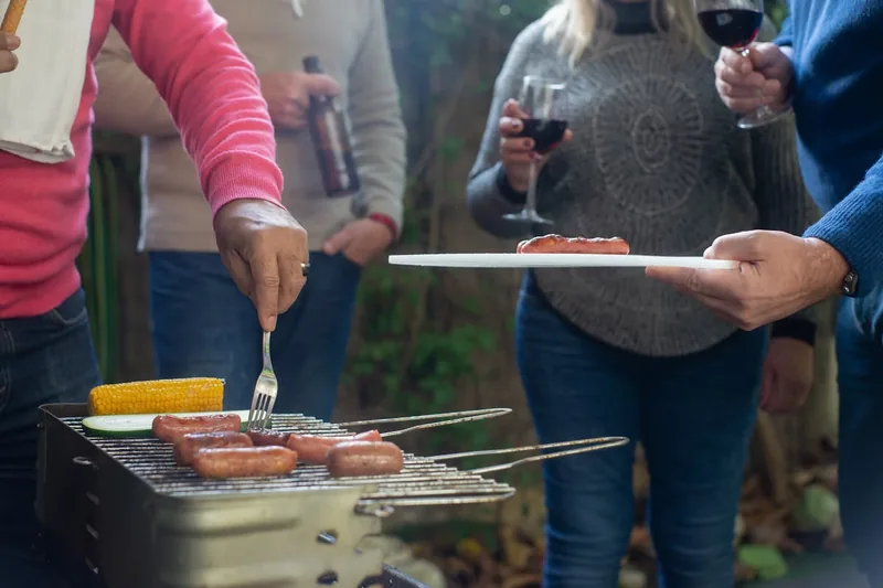 Eine sommerliche Gartenparty-Szene mit gedecktem Tisch, darauf appetitliches Grillgut und erfrischende Getränke, im Hintergrund ein Grill.