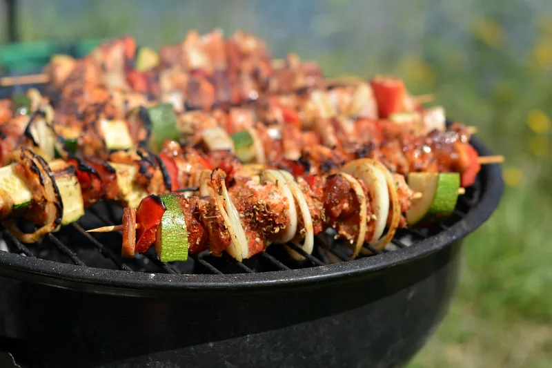 Entspannte Grill-Atmosphäre im Park mit fertigem Grillgut und einem Grilleimer im Hintergrund.