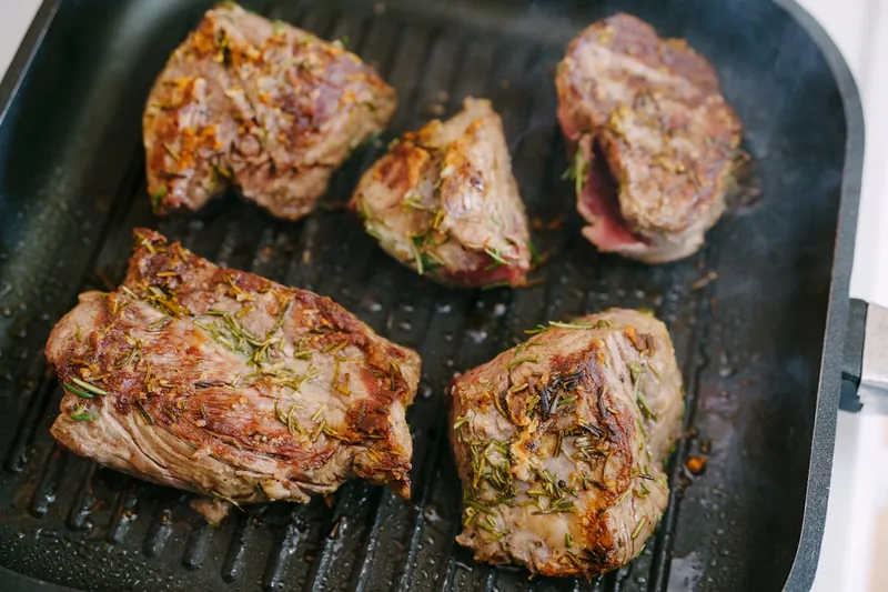 Eine Hand wendet ein saftiges Steak in einer heißen Steakpfanne, um perfekte Grillstreifen zu erzielen.