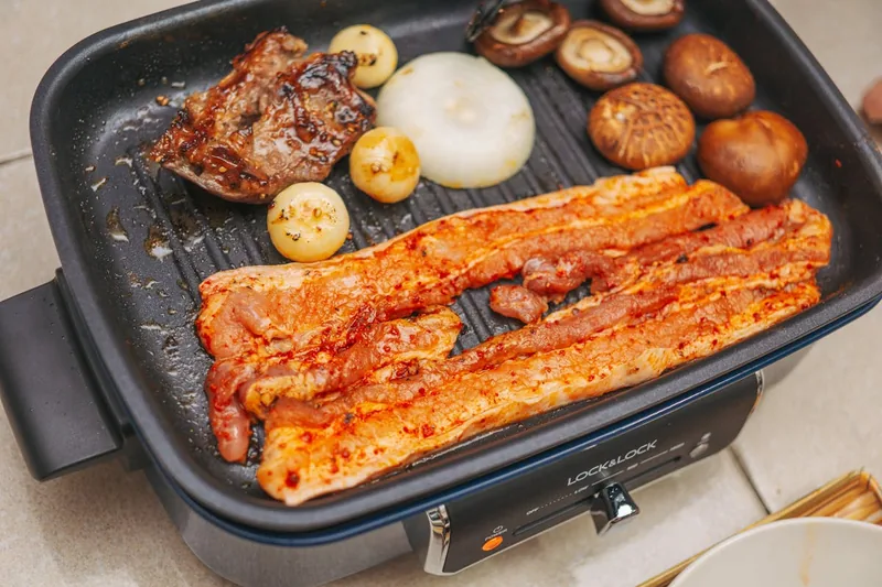 Eine Person brät frisches Gemüse auf einer Grillplatte. Eine Hand ist beim Wenden des Essens zu sehen.
