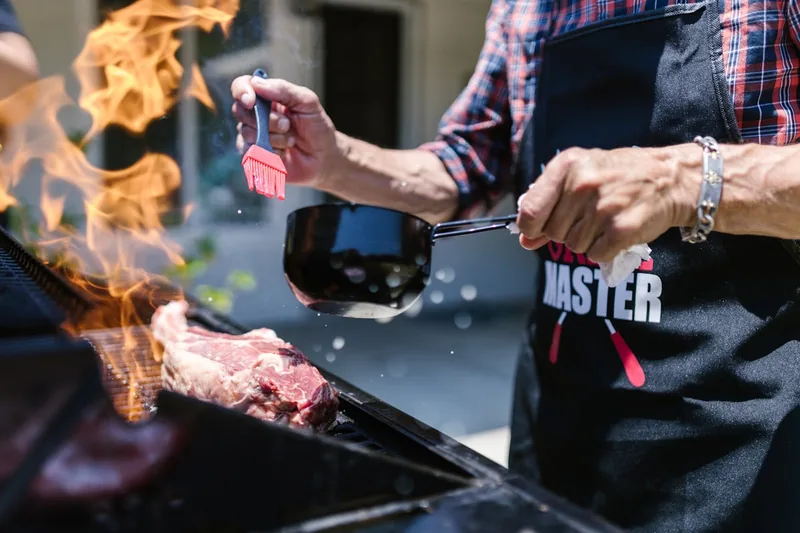 Ein Grillmeister trägt eine schützende Grillschürze, während er Steaks auf dem Holzkohlegrill zubereitet.