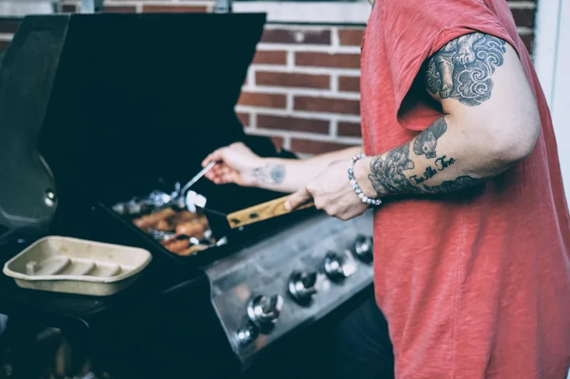 Eine Person bereitet auf dem Seitenkocher eines Grillwagens Beilagen zu, während der Hauptgrill läuft.