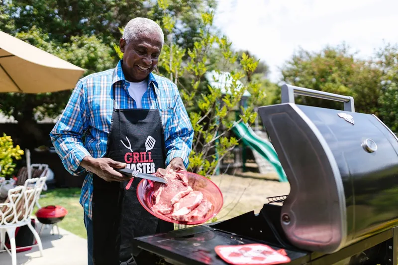 Fröhliche Gruppe feiert ein Grillfest im Garten, der Grillwagen steht im Hintergrund bereit.