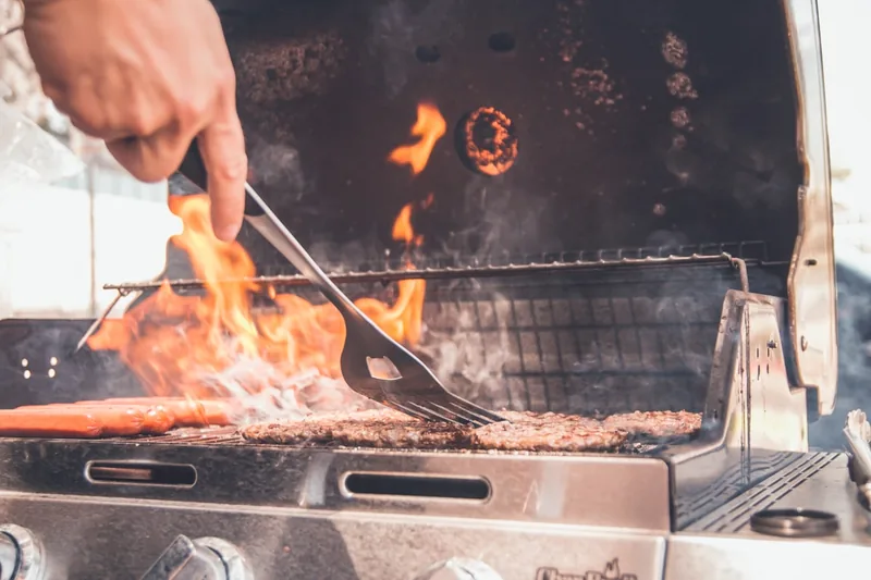 Eine Hand wendet mit einem Grillwender ein saftiges Steak auf einem heißen Holzkohlegrill.
