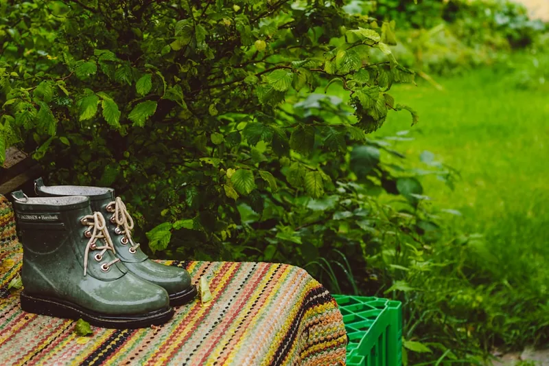 Ein Paar Gummistiefel steht nach der Gartenarbeit im sonnigen Garten, Symbol für Komfort und Funktionalität.
