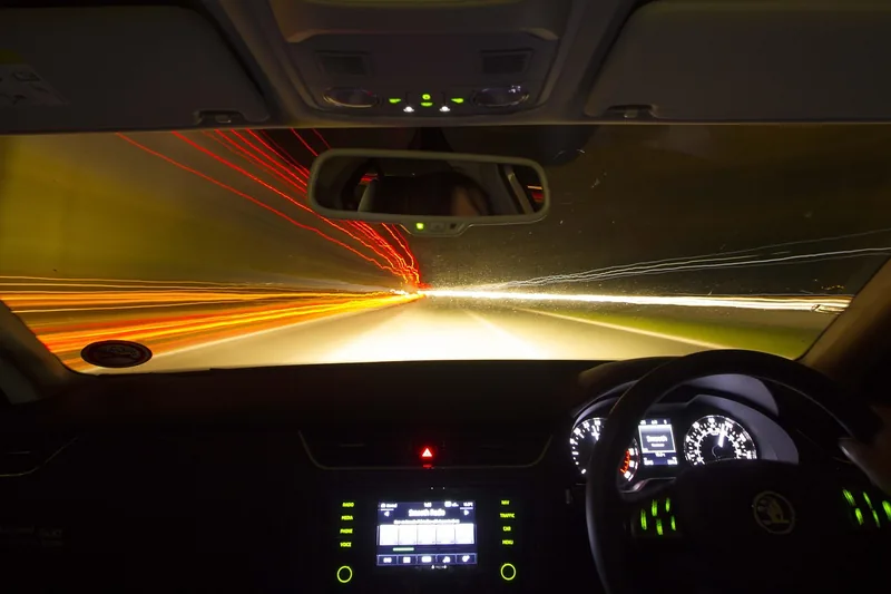 Ein Auto fährt nachts auf einer Straße, heller Lichtkegel der H1-Scheinwerfer leuchtet die Fahrbahn aus.