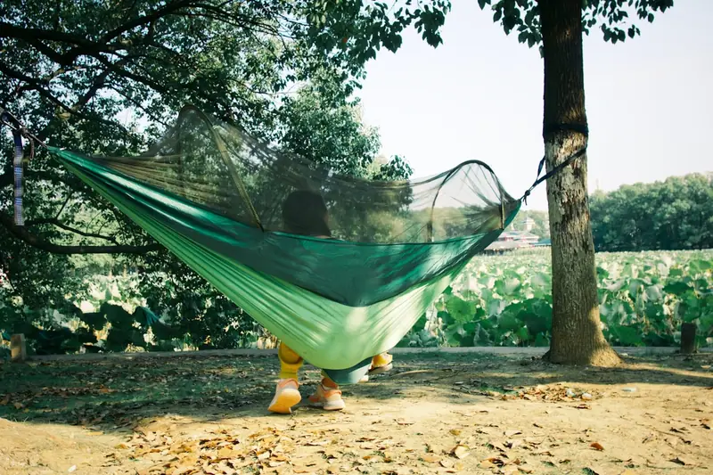 Eine Person entspannt in einer Camping Hängematte mit Moskitonetz, geschützt im Grünen liegend.