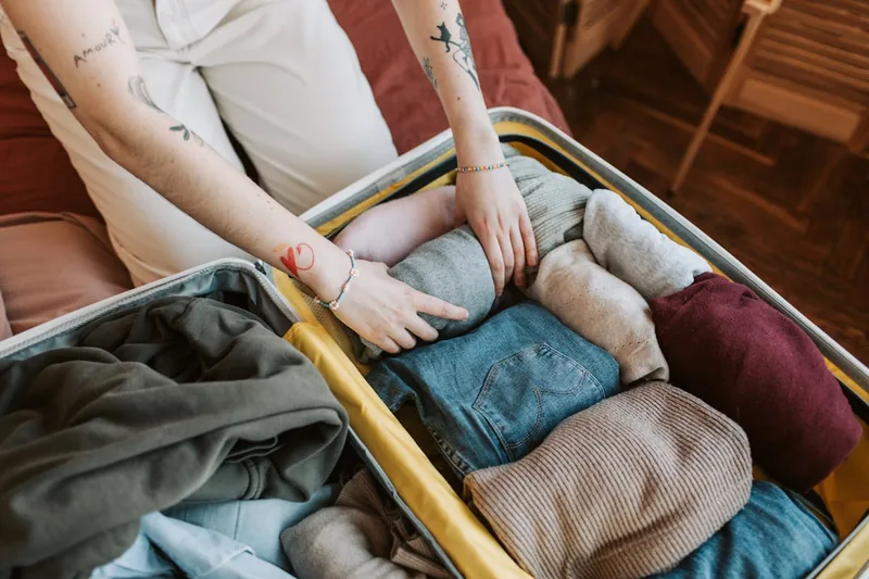 Eine Person faltet sorgfältig Kleidung, um sie effizient in einen offenen Handgepäck-Koffer zu packen.