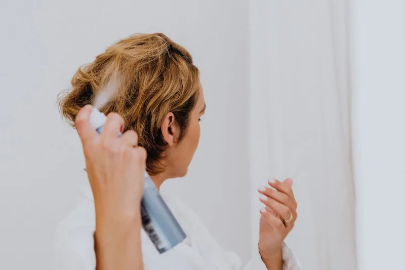 Eine Person sprüht Hitzeschutzspray auf ihr Haar vor dem Styling, schützt es vor Hitze.