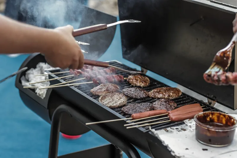 Eine Hand legt Grillgut auf einen in Betrieb befindlichen Holzkohlegrill mit Aktivbelüftung.