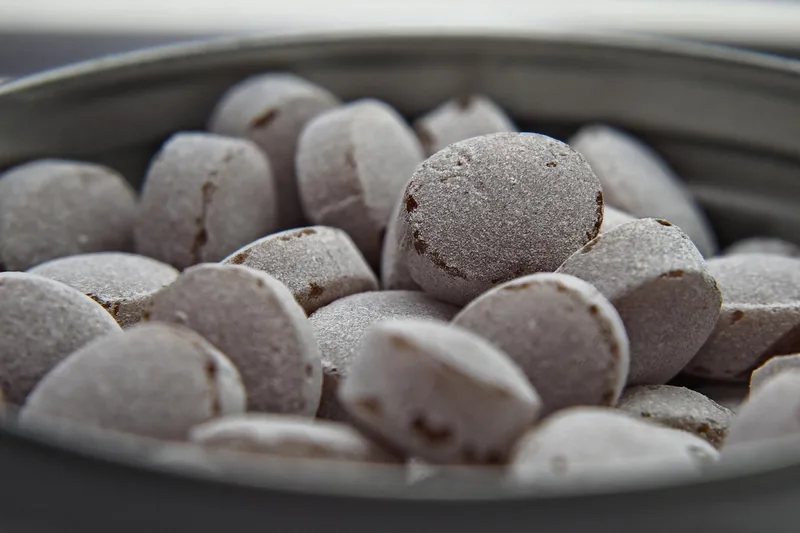 Eine Hand nimmt ein Hustenbonbon aus der Packung, um es gegen Hustenreiz anzuwenden und die Wirkstoffe zu nutzen.