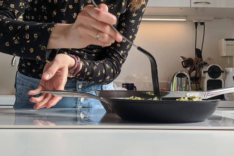 Eine Hand brät Gemüse in einer Induktionspfanne auf einem modernen Induktionskochfeld.