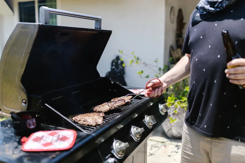 Eine Person wendet saftiges Steak auf einem Infrarotgrill im Garten, während Rauch aufsteigt.
