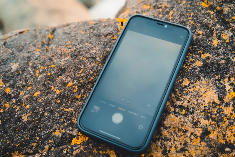 Eine Person benutzt ein iPhone 12 in robuster Outdoor-Hülle auf einem schmalen Wanderweg.