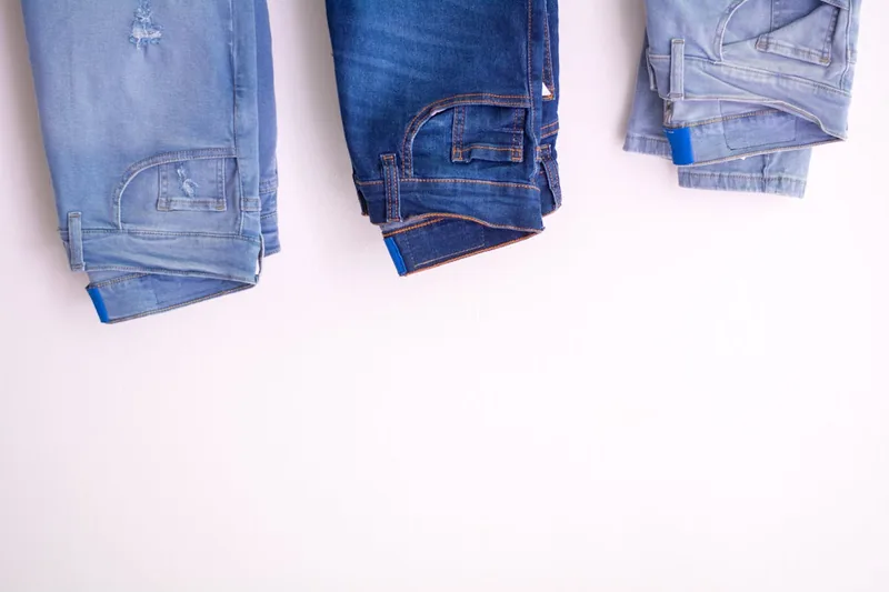 Eine sauber gefaltete Herren Jeanshose in klassischem Blau, isoliert auf neutralem Hintergrund, bereit zum Anprobieren.