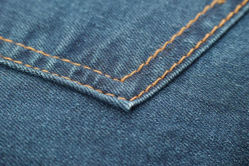 Nahaufnahme des robusten Denim-Materials einer Jeanshose für Herren, zeigt die feine Webstruktur und die Nahtdetails.
