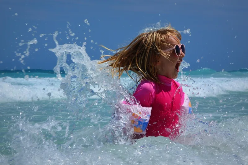 Fröhliche Kinder spielen an einem sonnigen Strand, eine Schwimmweste liegt als Zeichen der Sicherheit bereit.