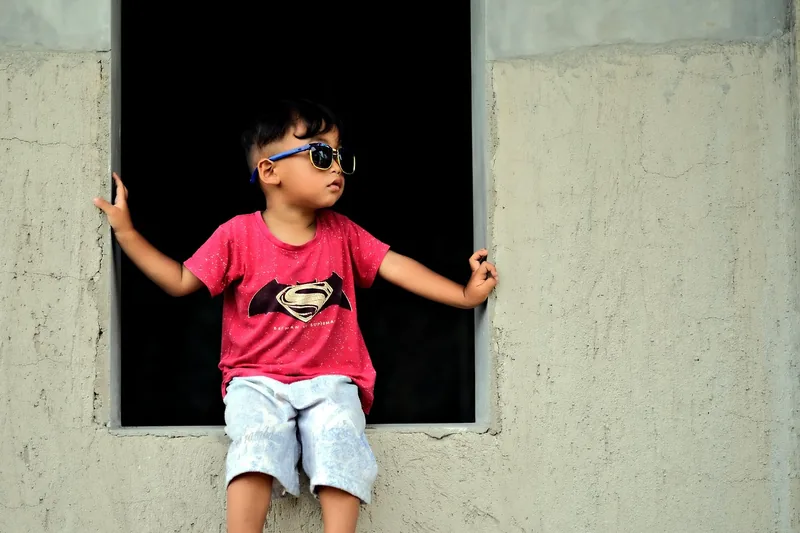 Ein lachendes Kind mit einer stilvollen Kinder-Sonnenbrille im Freien spielend, von der Seite aufgenommen.