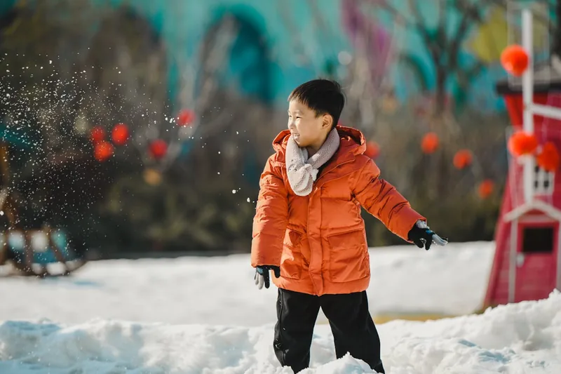 Ein Kind lachend im Schnee spielend, geschützt und warm in seiner farbenfrohen Kinder-Winterjacke.