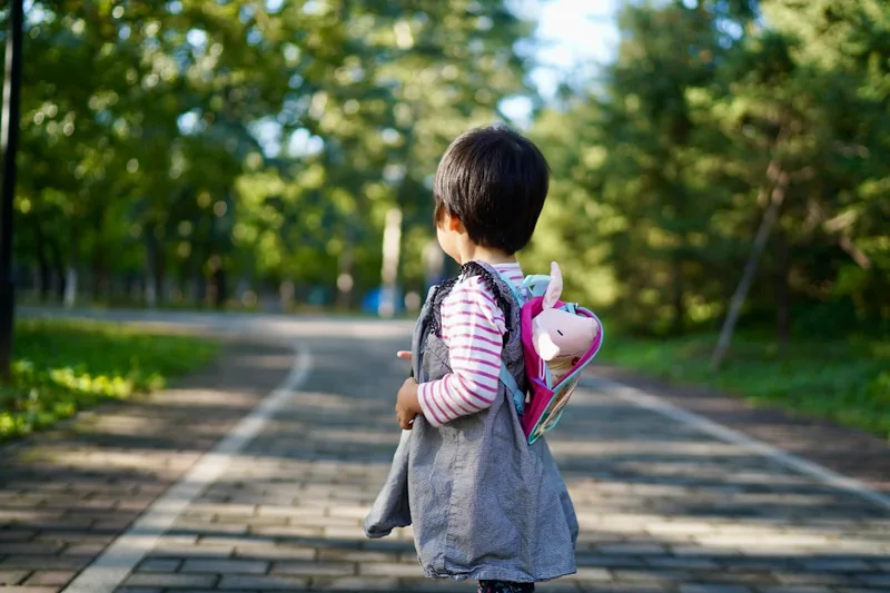Ein Kind trägt seinen farbenfrohen Kinderrucksack auf dem Rücken beim Spaziergang im Park.