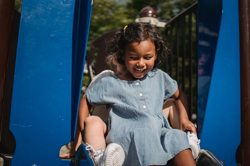 Ein kleines Kind rutscht lachend eine sichere Kinderrutsche hinunter, fokussiert auf Spielspaß.