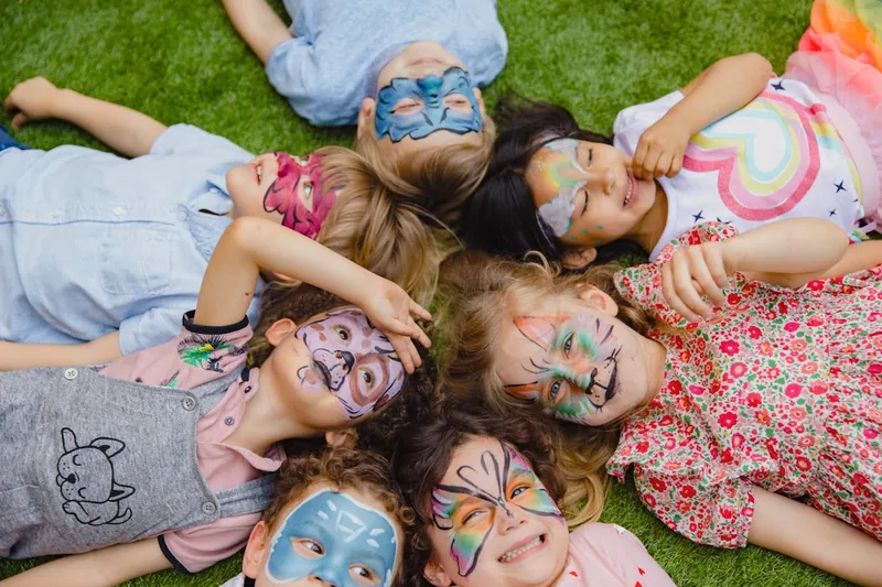 Fröhliche Kinder mit kunstvoll geschminkten Gesichtern spielen auf einem Kindergeburtstag, voller Freude und Kreativität.