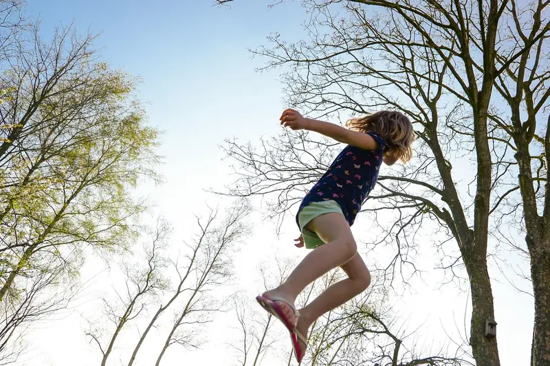 Ein Kind lachend beim sicheren Trampolinspringen auf einem Kindertrampolin im Garten.