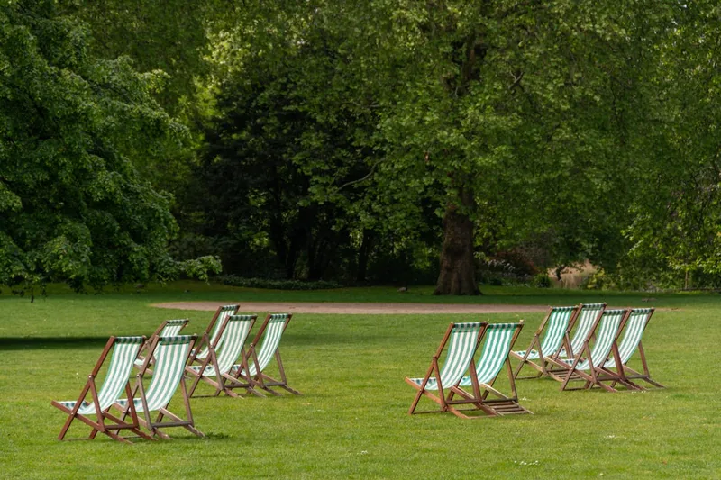 Eine sommerliche Gartenszene mit mehreren Klappsesseln, die zum Verweilen unter einem Baum einladen.