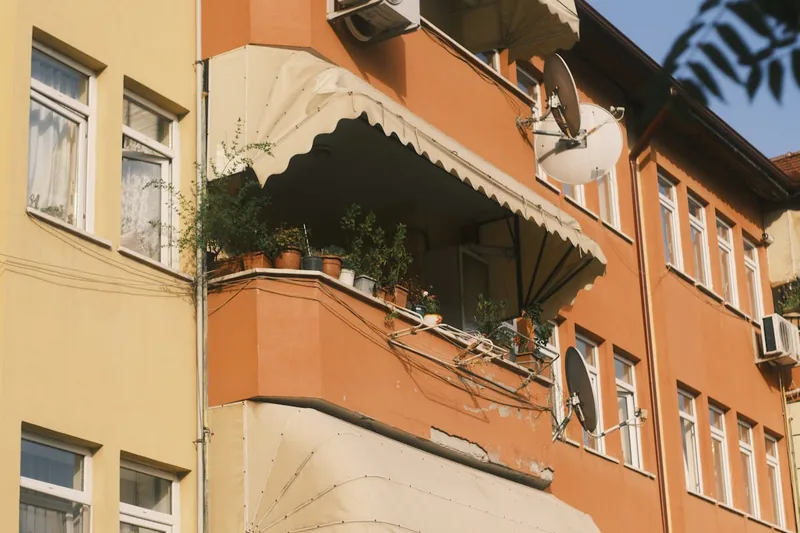 Eine Person verstellt die Neigung einer Klemmmarkise auf einem Balkon zur optimalen Beschattung.